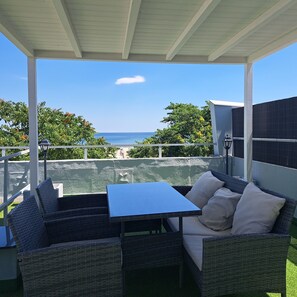 Un patio techado con muebles de mimbre y una mesa, con vistas a un cuerpo de agua y follaje.