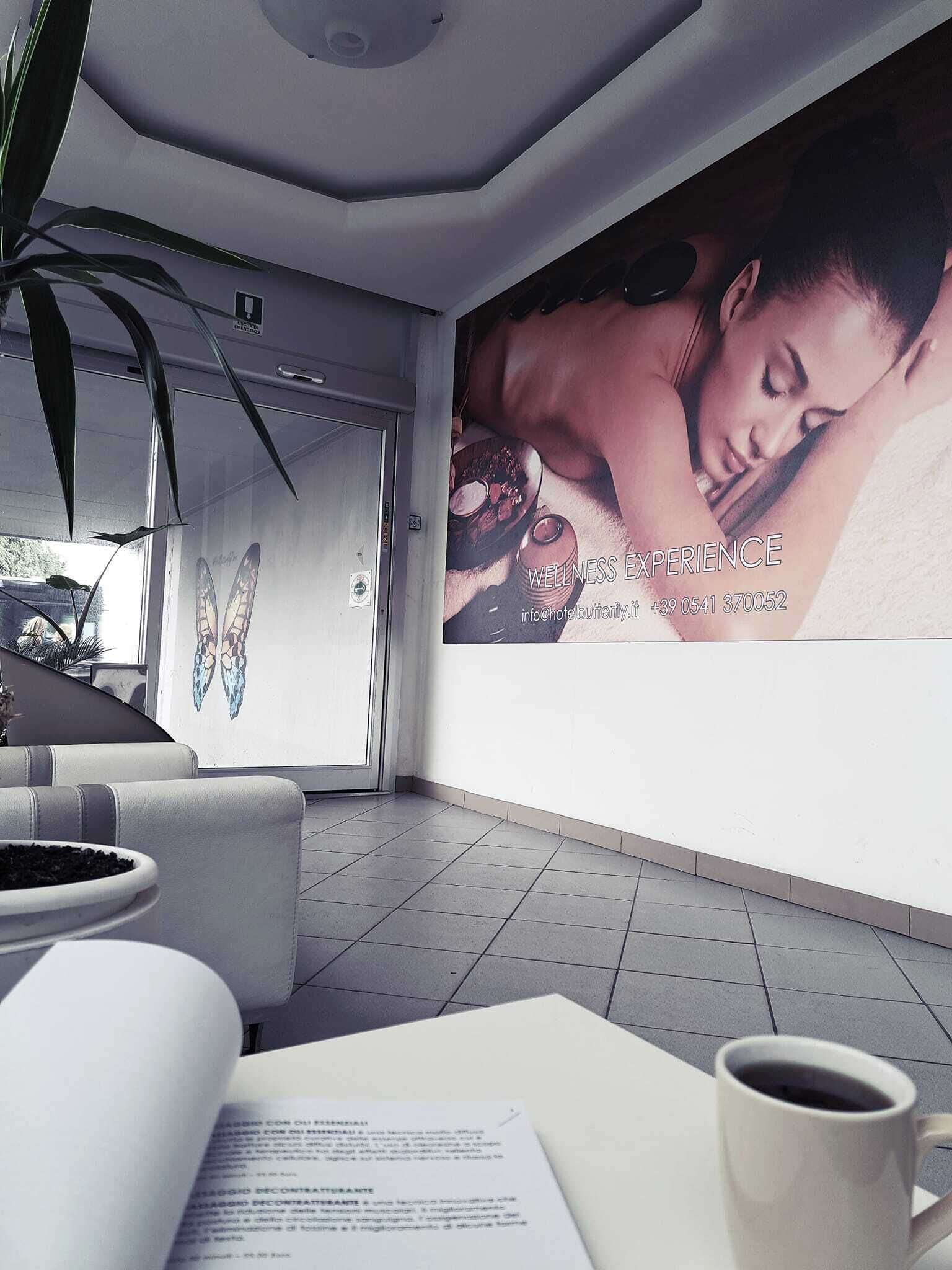 Un hall d’hôtel moderne, avec une grande affiche présentant les services de bien-être, un coin salon avec une table basse et une plante en pot.