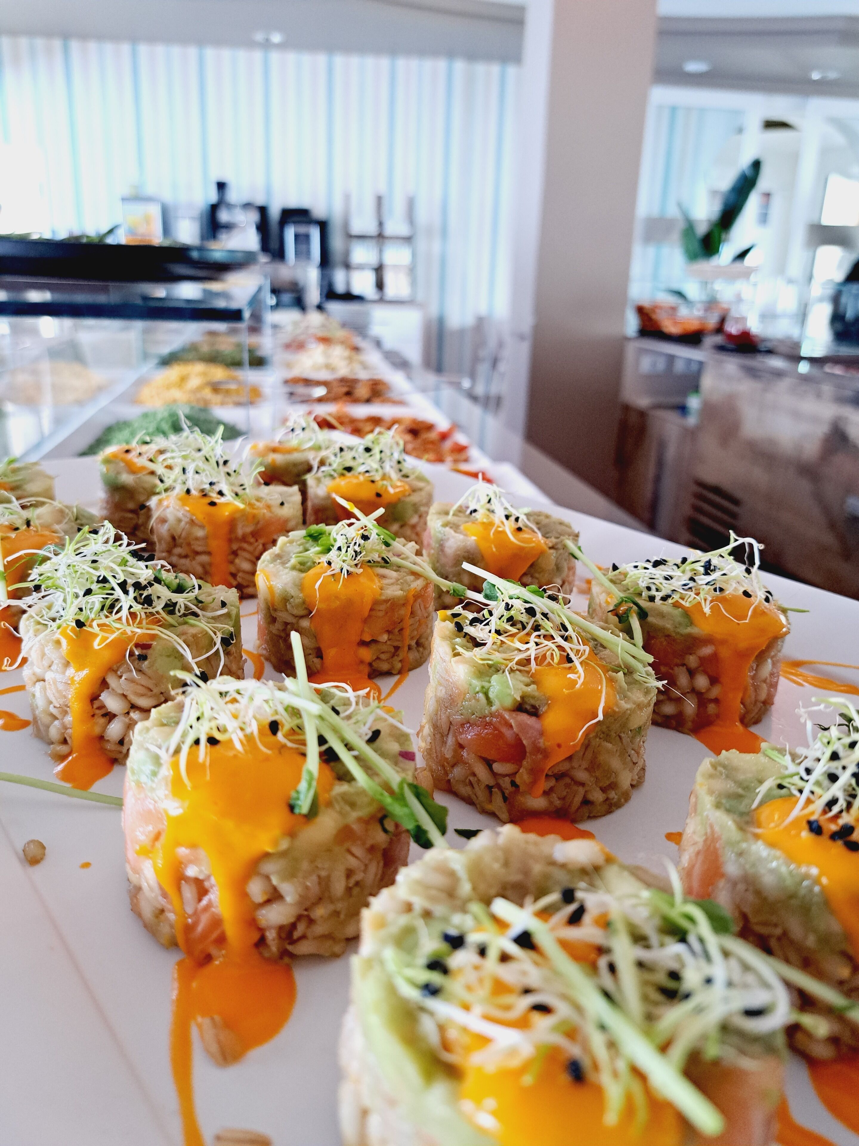 A long table with neatly arranged food items, likely a buffet or appetizer spread, in a modern dining area with a bright, airy atmosphere.