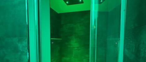 Una habitación con paredes de vidrio, techo iluminado en verde y un ventanal pequeño.