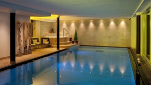 An indoor swimming pool with a clear water surface, a reception area with a counter and seating, and a staircase leading to a higher level. - Hotel Italia (Corvara in Badia)