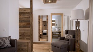A modern living room with a wooden accent wall, a grey sofa, a matching armchair, and a floor lamp. - Hotel Italia (Corvara in Badia)
