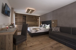 A modern bedroom with a bed, a sofa, a desk, and a TV. - Hotel Italia (Corvara in Badia)