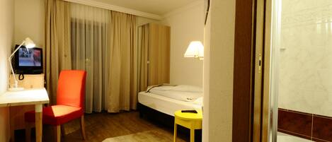 Une chambre d’hôtel comprenant un lit, un bureau avec une chaise, une télévision, une lampe, ainsi qu’une salle de bain avec des toilettes et un lavabo.