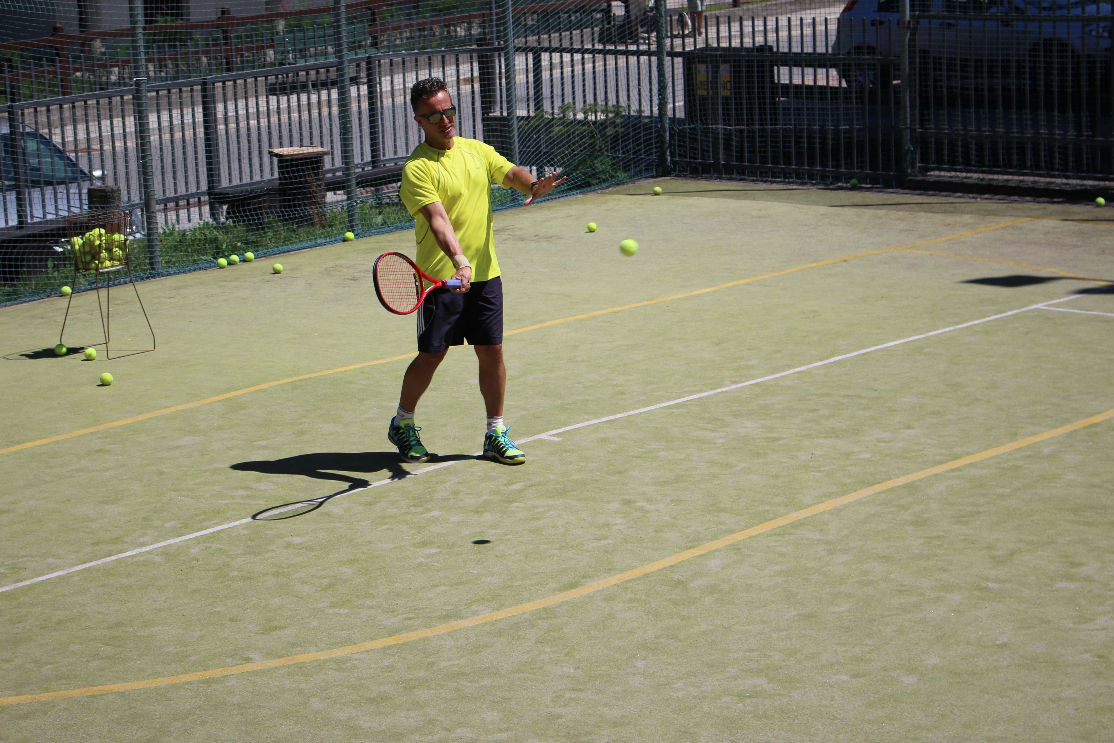A tennis court with a net, a player in a yellow shirt, and tennis balls scattered around.