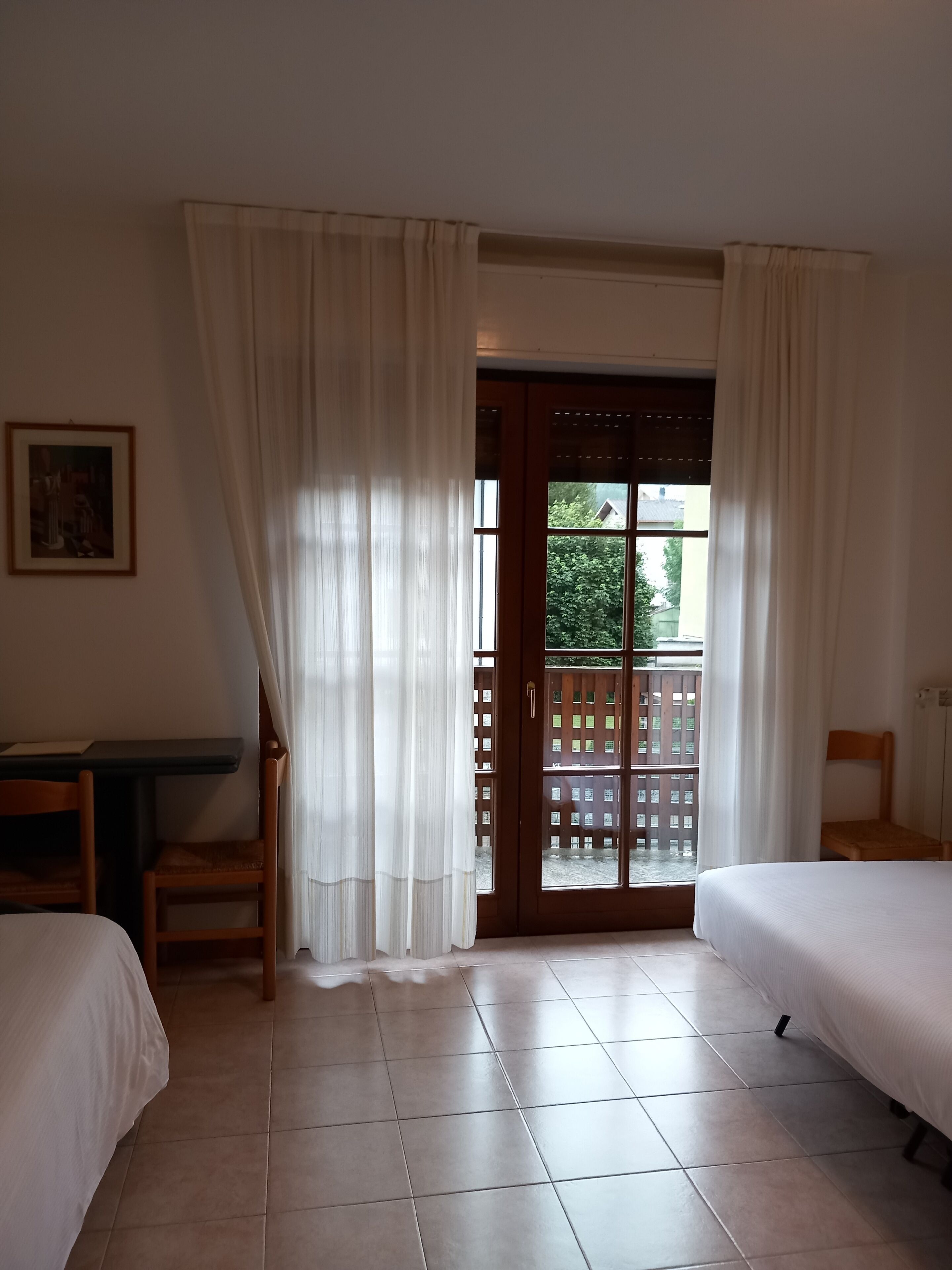 Quarto de hotel com uma cama, uma escrivaninha, uma cadeira e vista para uma varanda através de uma porta de vidro.
