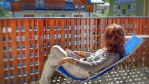 A person sitting on a lounge chair on a balcony with a view of buildings and mountains. - Residence Biancaneve (Aprica)