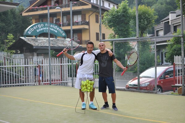 A tennis court with a net, a sign reading "albergo residency", and a car parked nearby. - Residence Biancaneve (Aprica)