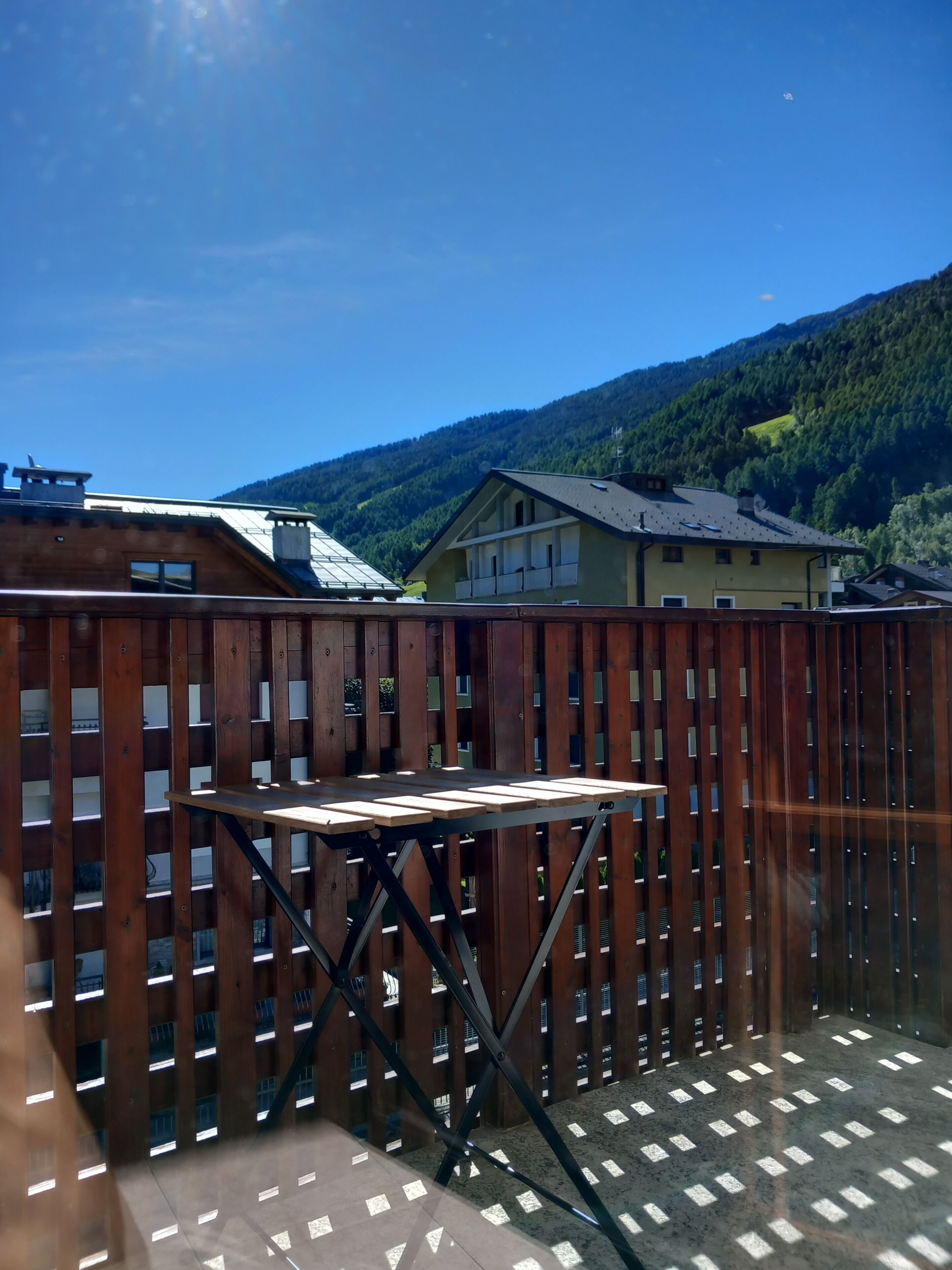 A wooden deck with a table, surrounded by a wooden fence, overlooking a mountainous landscape.