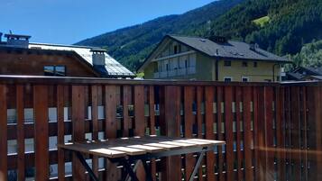 A wooden deck with a table, surrounded by a wooden fence, overlooking a mountainous landscape.