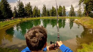 A person fishing by a calm lake surrounded by trees.