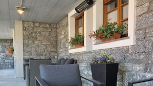 A covered outdoor seating area with stone walls, wicker furniture, and potted plants. - Residence Biancaneve (Aprica)