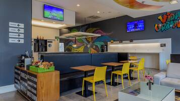 Um restaurante moderno com área de bar, assentos e uma tela de televisão.