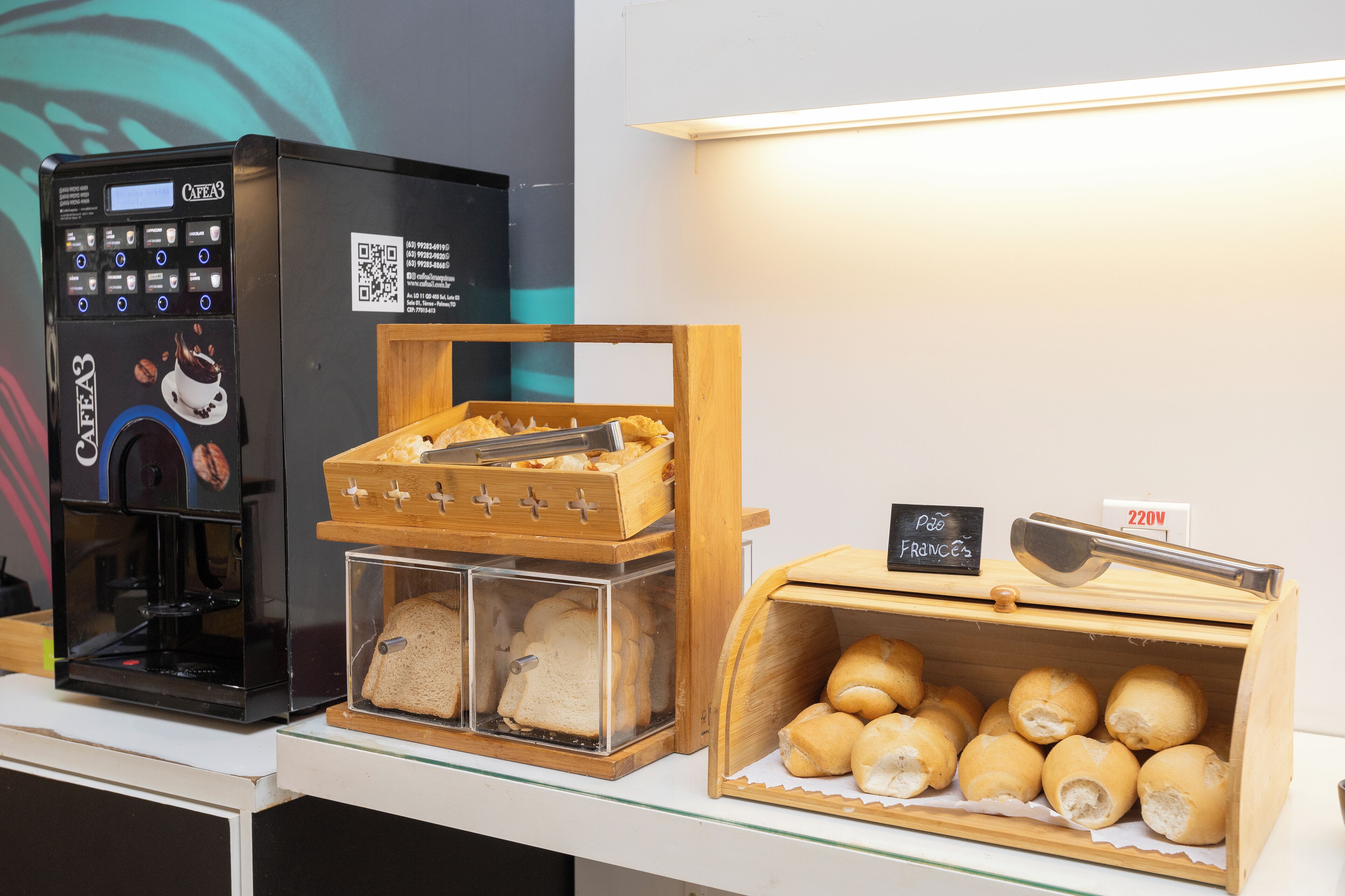 Una máquina de café, una vitrina con pan y una caja de pasteles con un letrero que indica un precio de 220V.