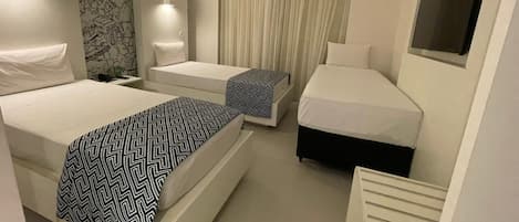 Une chambre d’hôtel avec deux lits, un bureau, une chaise, une télévision et un rideau.
