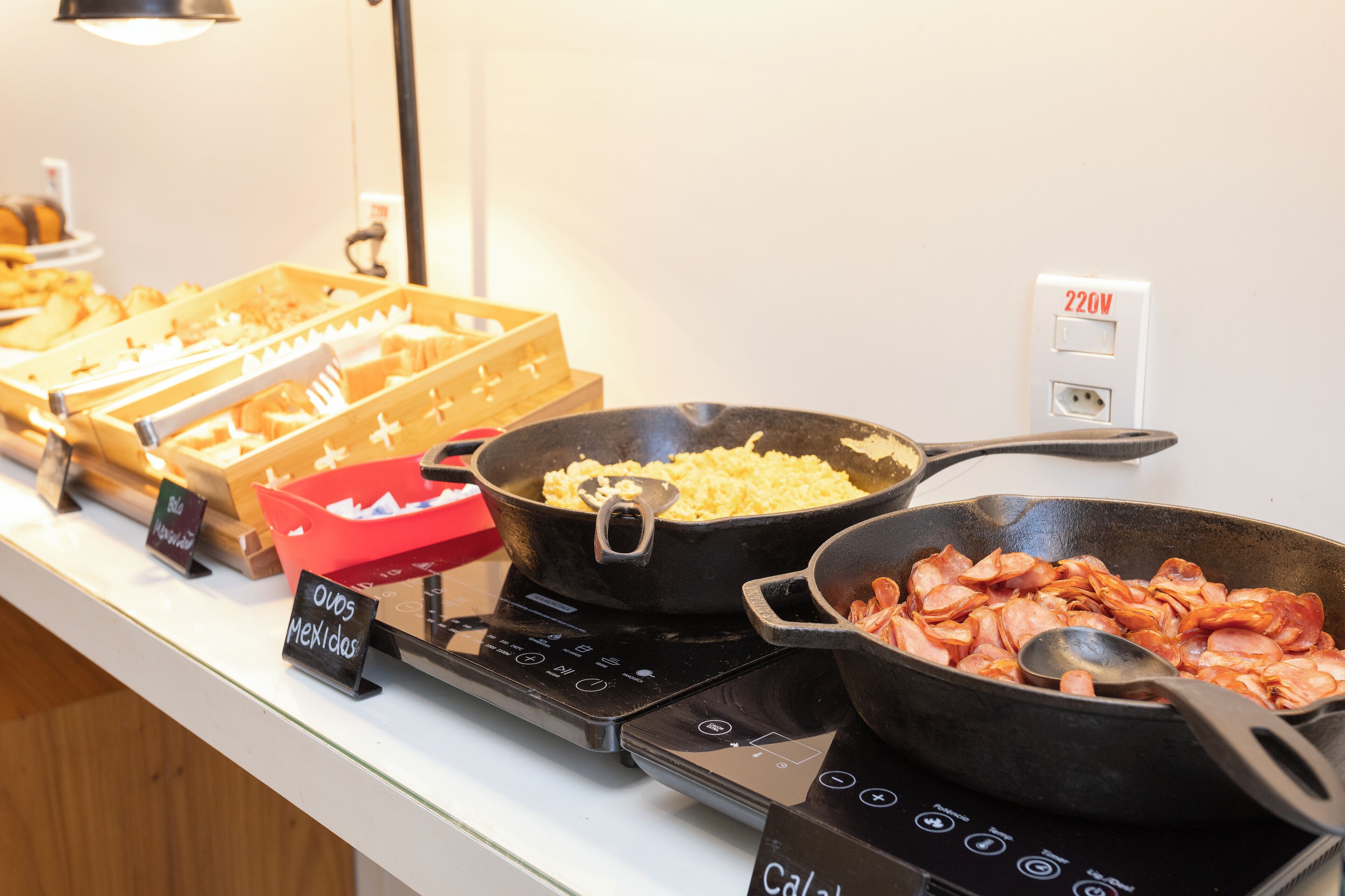 A buffet with various dishes including a pan of scrambled eggs, a pan of bacon, and a tray of nachos.
