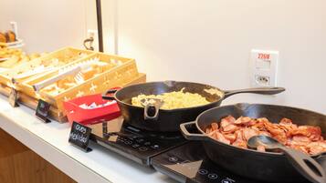 A buffet with various dishes including a pan of scrambled eggs, a pan of bacon, and a tray of nachos.