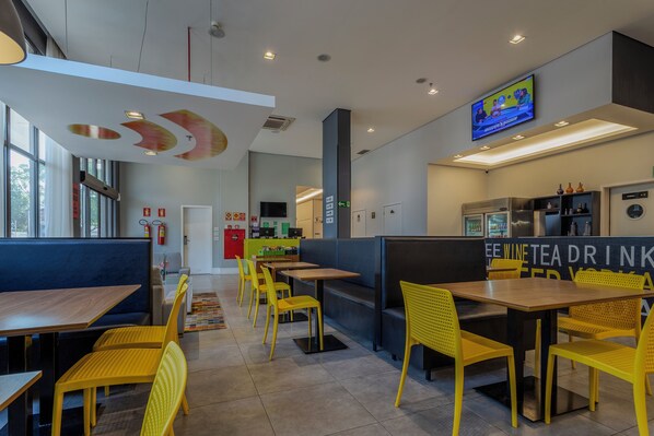 A modern restaurant interior with yellow chairs, wooden tables, and a TV mounted on the wall. - Nacional Inn Palmas (Palmas)