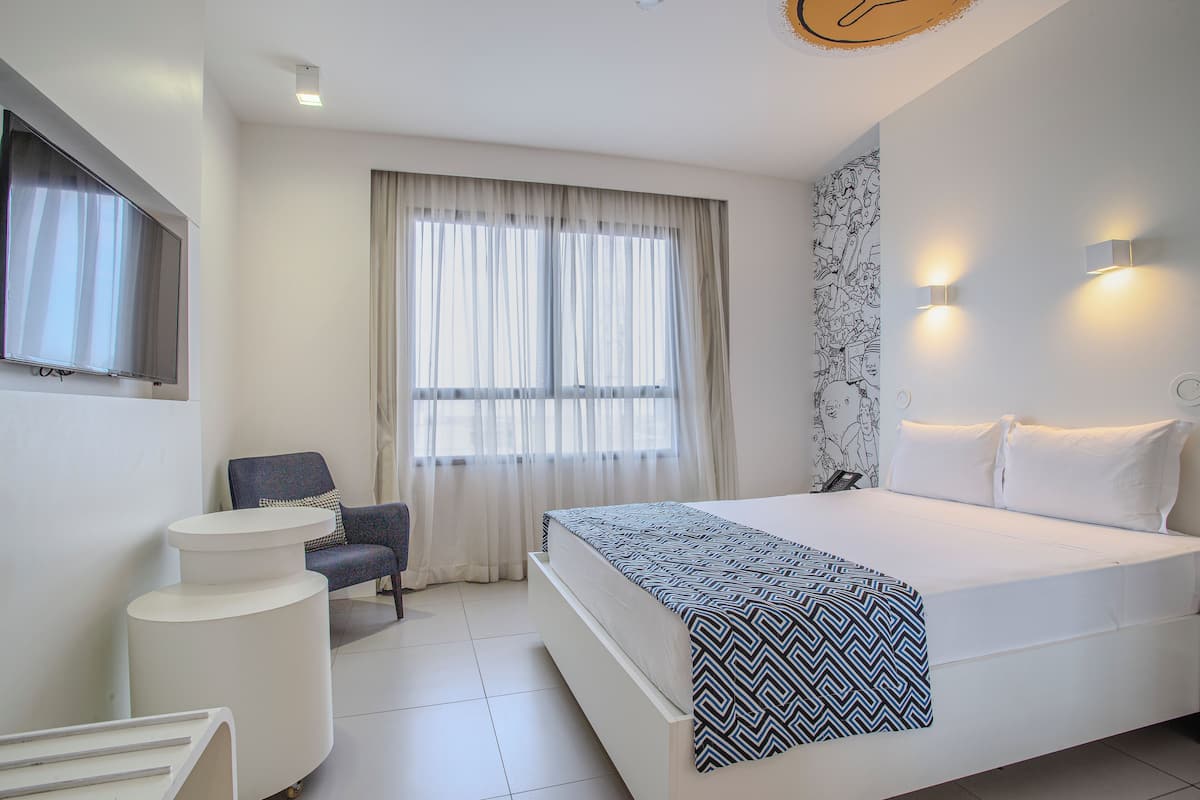 Ein modernes Hotelzimmer mit Bett, Stuhl, Schreibtisch und einem Fenster mit Vorhängen.