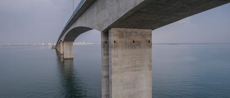 A concrete bridge over calm water with a distant city skyline.