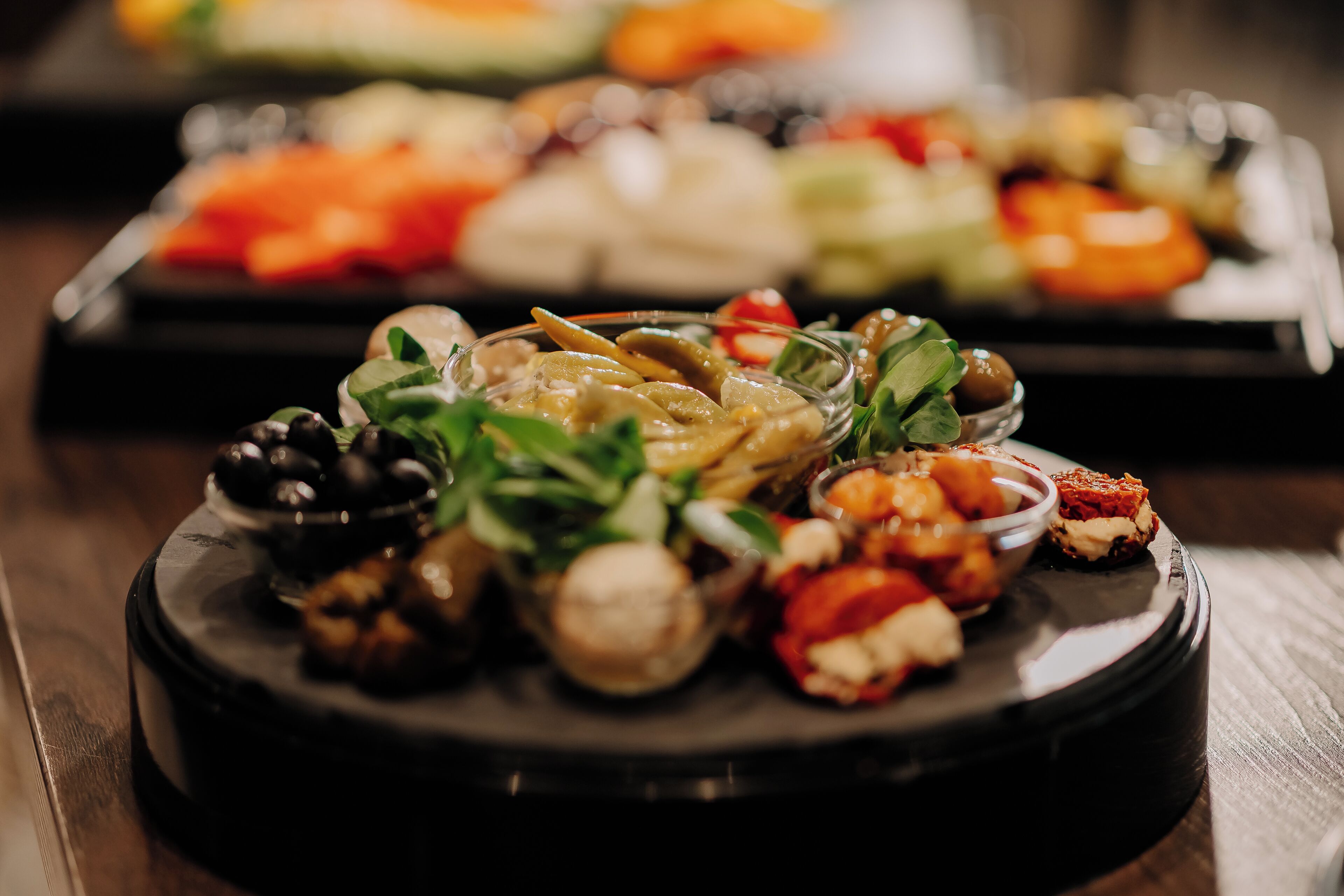 A variety of food items on a round serving tray, including olives, nuts, and vegetables.