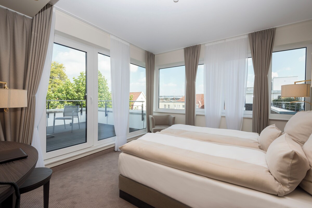 Quarto de hotel com cama, secretária e vista para o exterior.