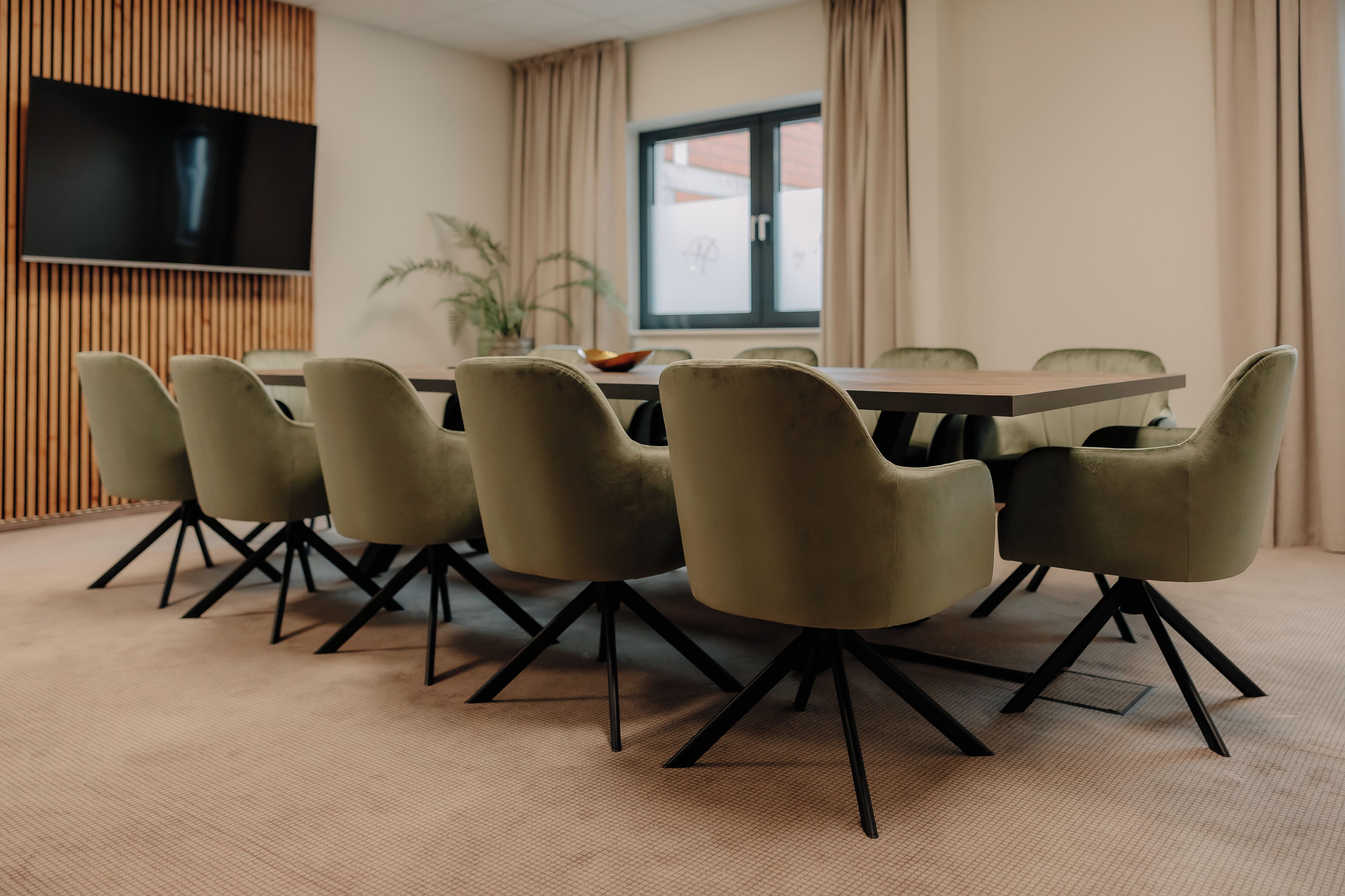 Un salón de conferencias con una mesa redonda, seis sillas, un televisor de pantalla plana montado en la pared y un ventanal con cortinas.