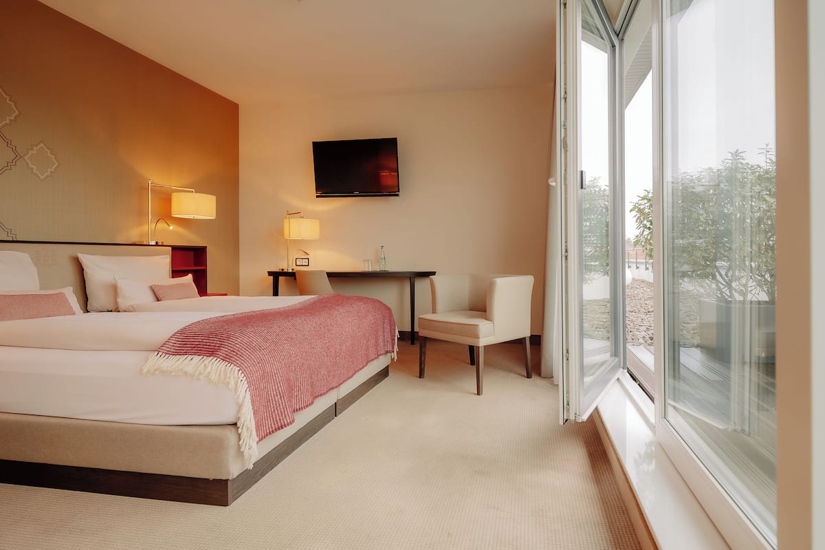 A hotel room with a large bed, a desk, a chair, a TV, and a window with a view.