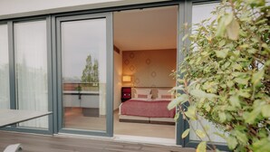 A bedroom with a bed, a nightstand, and a lamp. There is a sliding glass door leading to a balcony with a table and chairs. - LOOKEN INN Lingen by Hackmann (Lingen)