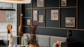 A modern living room with a grey sofa, a coffee table, and a side table with a lamp. There are framed pictures on the wall and a vase with flowers on the coffee table. - LOOKEN INN Lingen by Hackmann (Lingen)