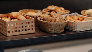 A buffet counter with baskets of bread and rolls, and stacks of plates. - LOOKEN INN Lingen by Hackmann (Lingen)