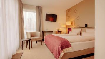 A hotel room with a bed, a chair, a desk, a TV, and a lamp.