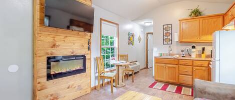 A cozy living area with a fireplace, wooden furniture, a dining table, and a kitchen with wooden cabinets.