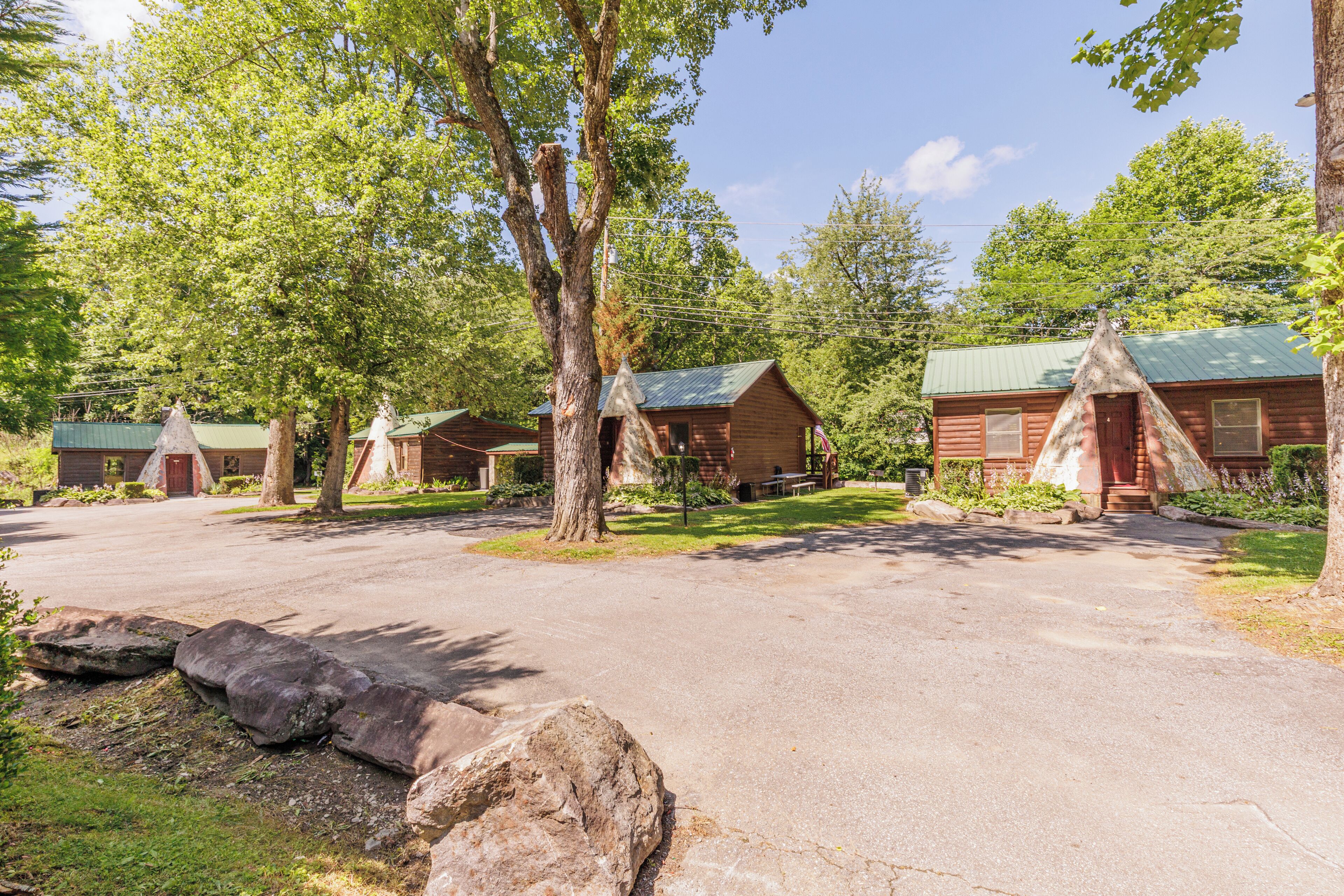 A campground with log cabins, a paved driveway, and surrounding trees.