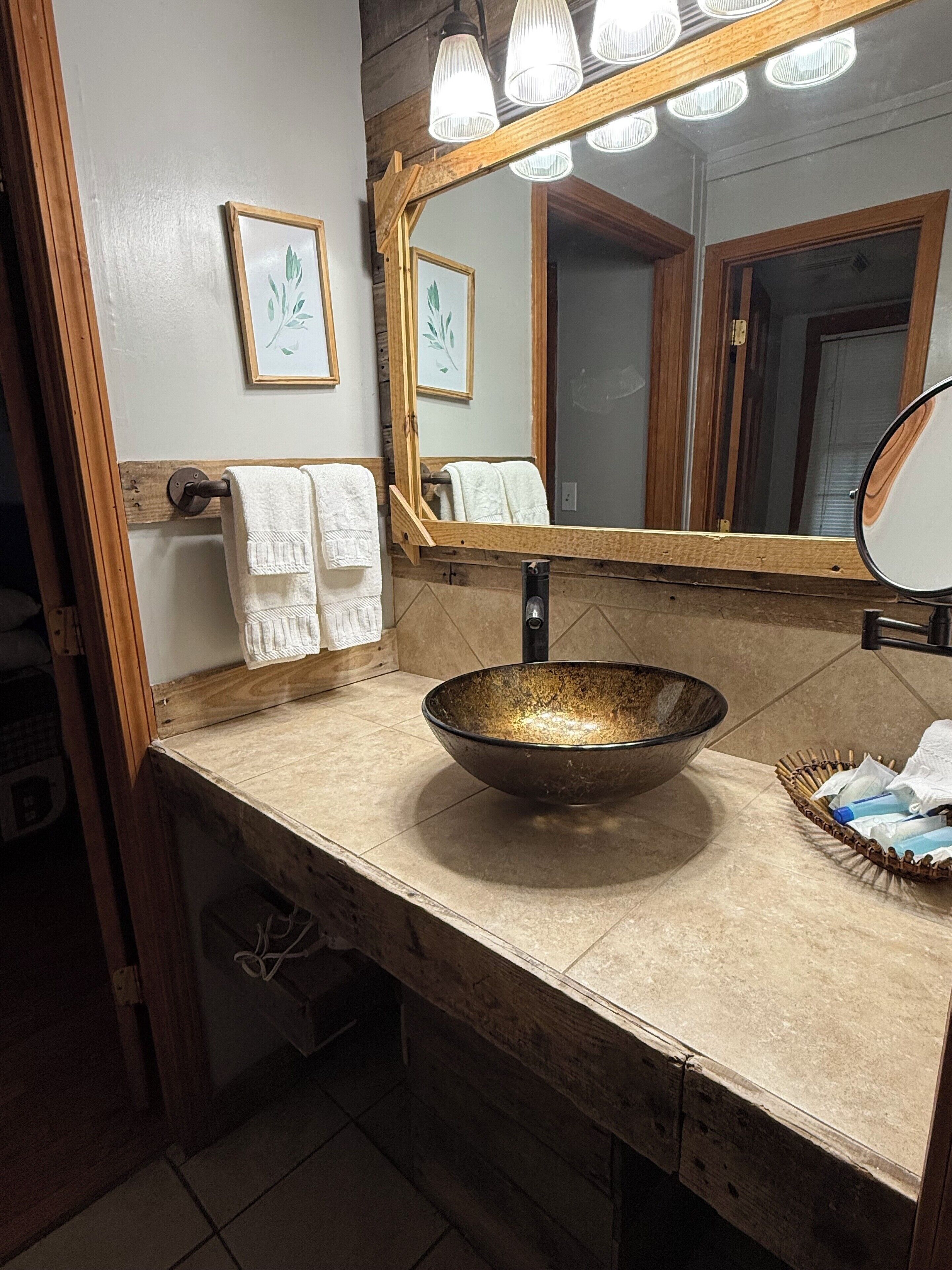 A bathroom with a wooden vanity, a large mirror, and a bowl sink.