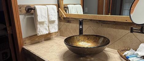 A bathroom with a wooden vanity, a large mirror, and a bowl sink.