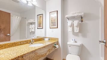 Uma casa de banho com lavatório de bancada em granito, um espelho, sanita e suporte para toalhas.