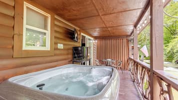 Une cabane en bois avec un jacuzzi sur la véranda, une télévision et une petite table avec des chaises.