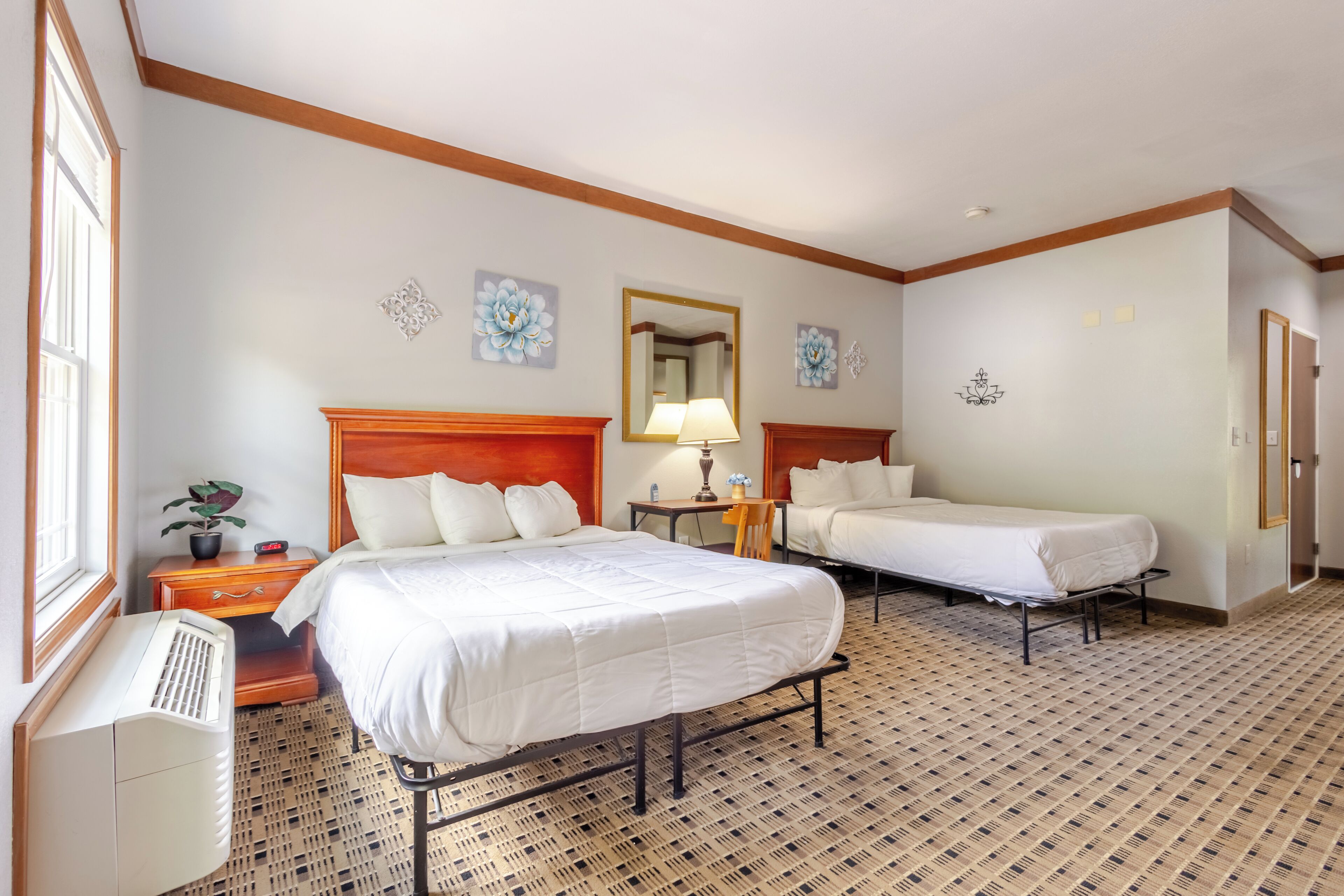 A hotel room with two beds, a wooden headboard, a nightstand with a lamp, and a potted plant.