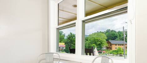 Habitación en esquina con ventana, una mesita, dos sillas y vistas a un edificio y árboles.