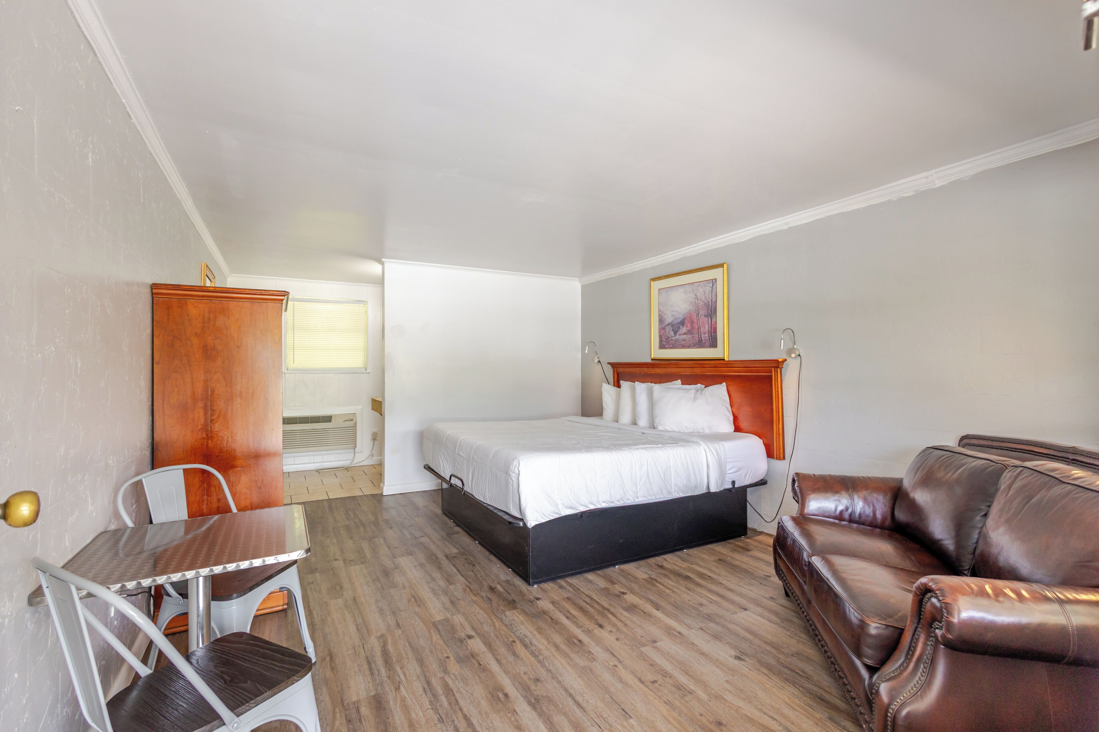 A hotel room with a bed, a leather sofa, a small table, and a chair.