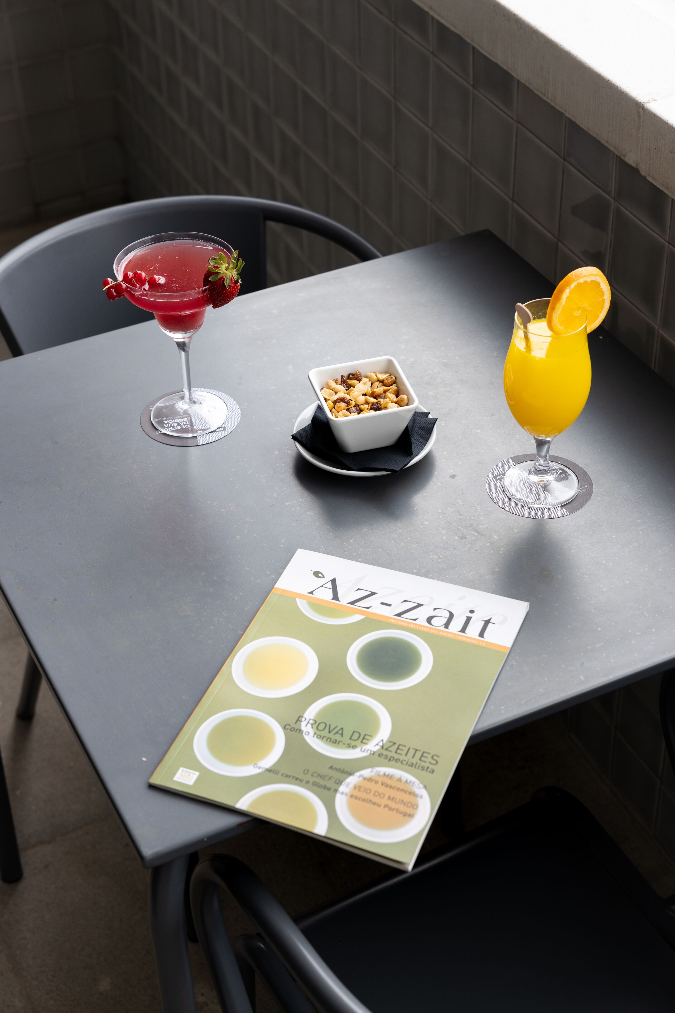 A table with a magazine, a bowl of nuts, and two drinks.