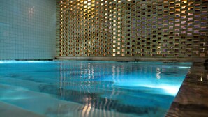 Una piscina interior con pared de azulejos y pared decorada con aberturas iluminadas.
