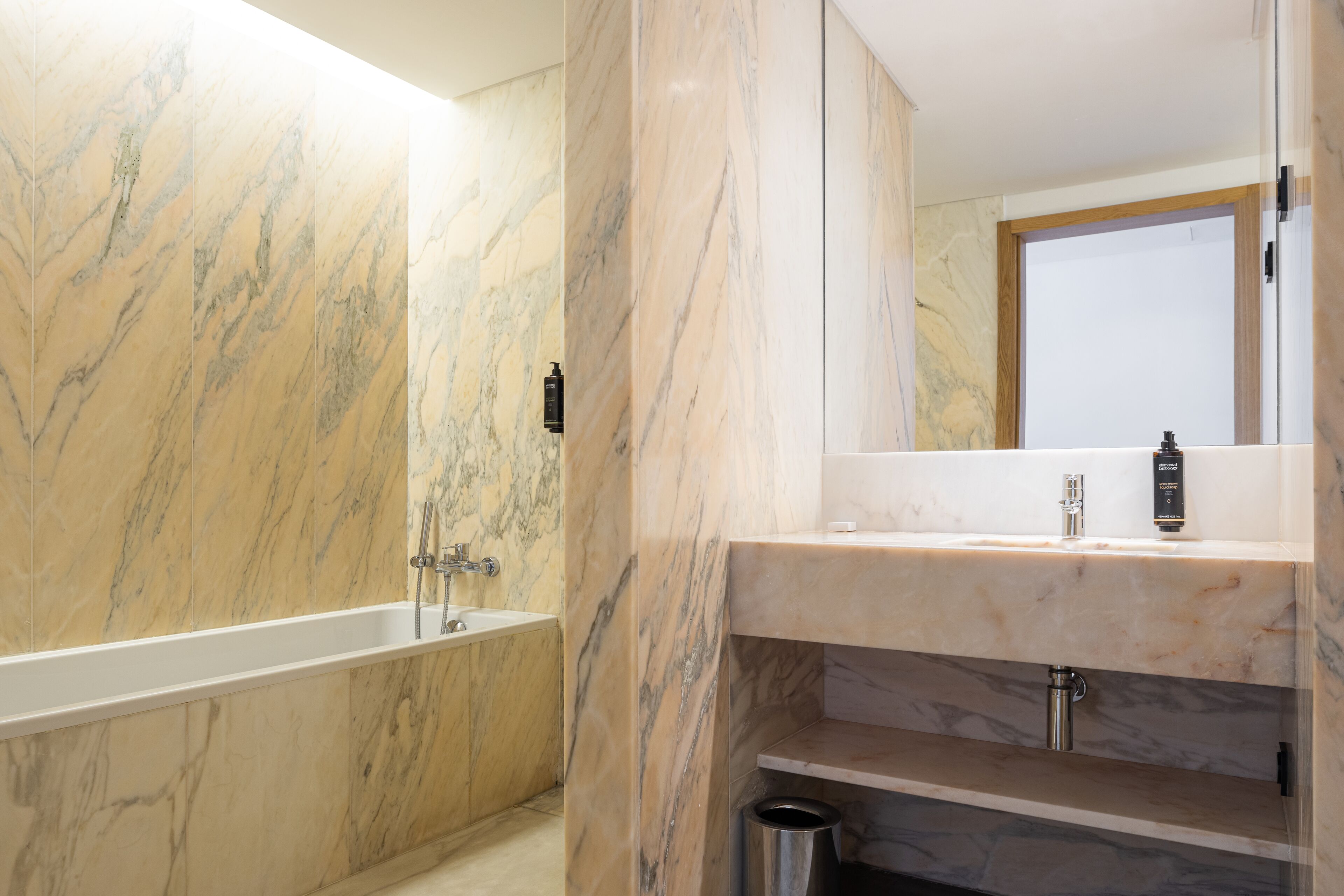 A modern bathroom with a marble wall, a bathtub, a sink, and a mirror.