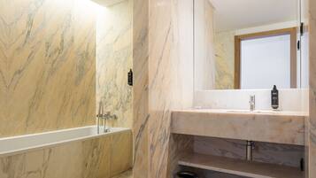 A modern bathroom with a marble wall, a bathtub, a sink, and a mirror.
