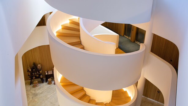 Una escalera en espiral de varios niveles con escalones de madera y paredes blancas, que conduce a diferentes plantas.