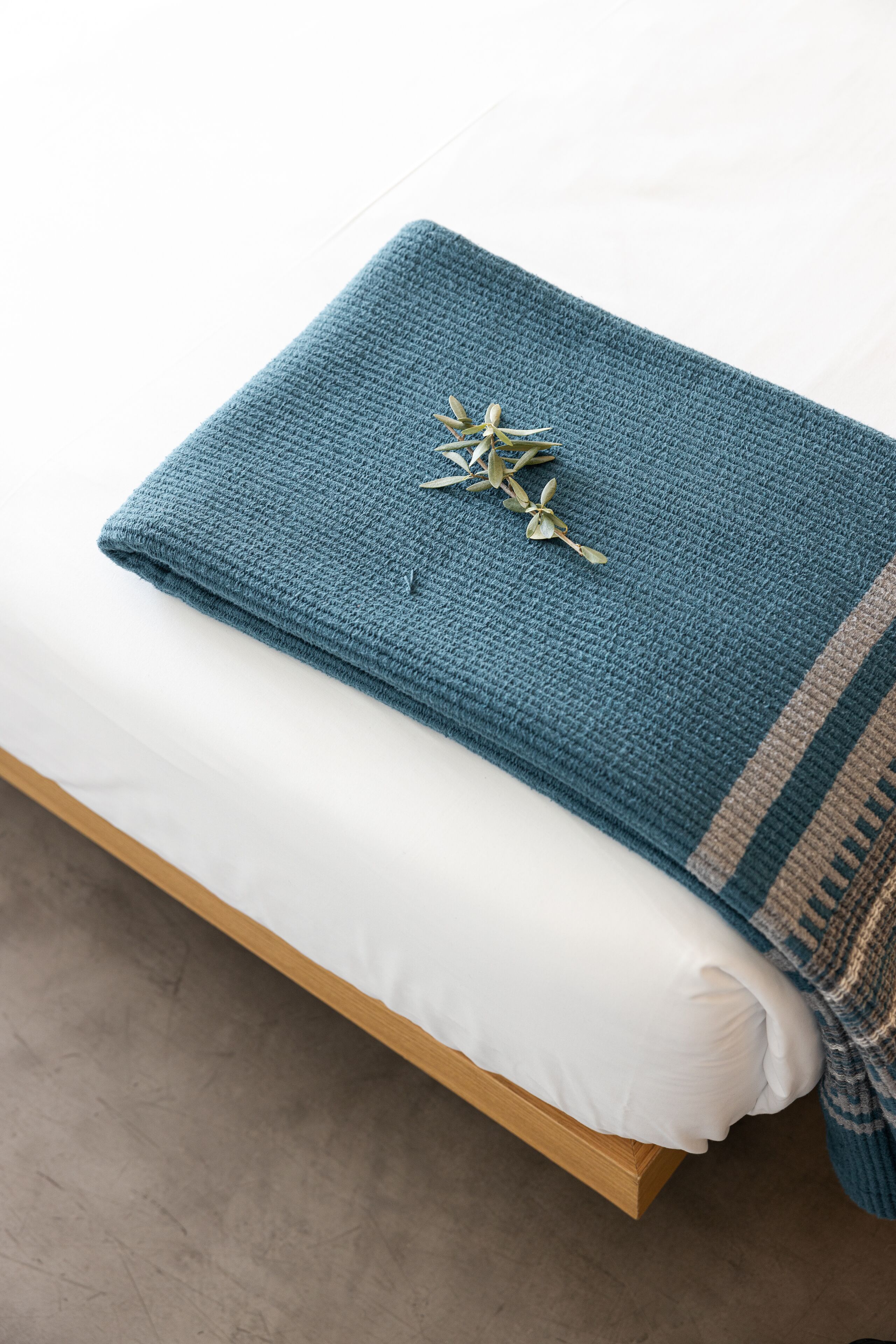 A neatly made bed with a blue blanket and a decorative item on top.