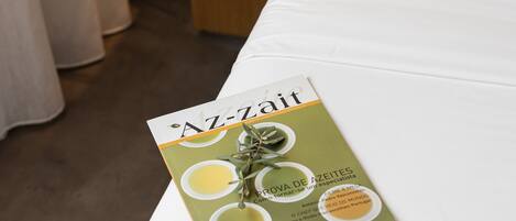 A hotel room with a wooden bedside table, a black telephone, and a brochure titled "Az-Zait".