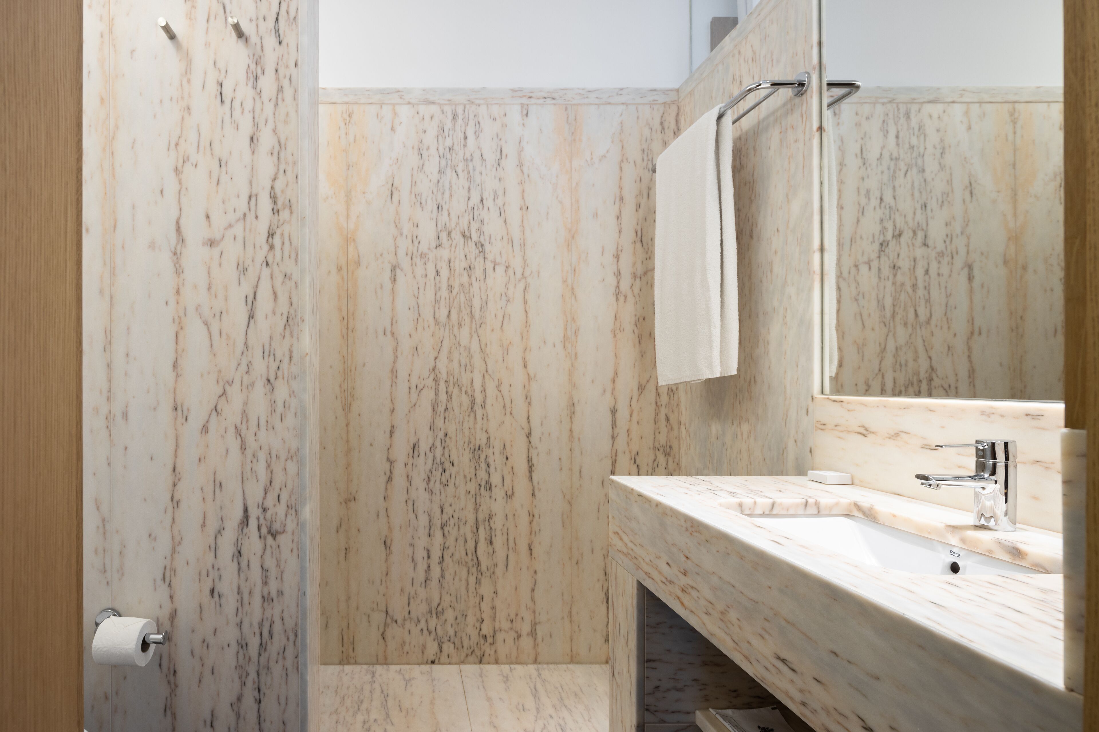 A bathroom with a marble wall, a sink, a mirror, and a towel rack.