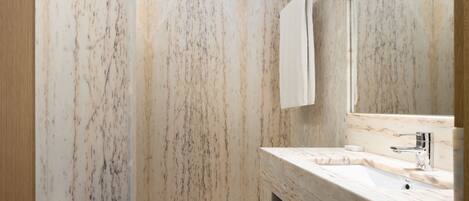 A bathroom with a marble wall, a sink, a mirror, and a towel rack.